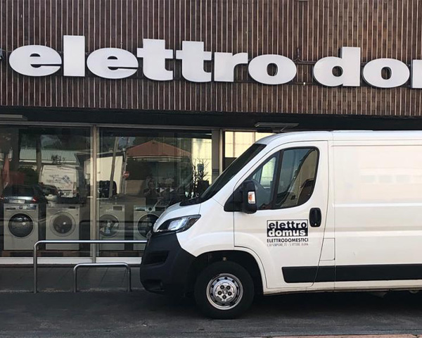 Foto dell'esterno dello storico negozio di elettrodomestici Elettrodomus. Nella foto si vede il negozio, la scritta e il furgoncino con il logo